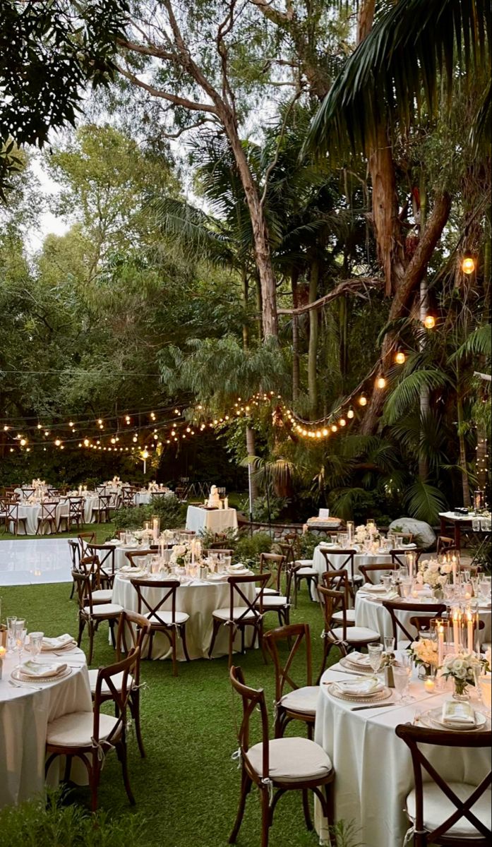 tables and chairs are set up for an outdoor dinner in the grass with lights strung over them