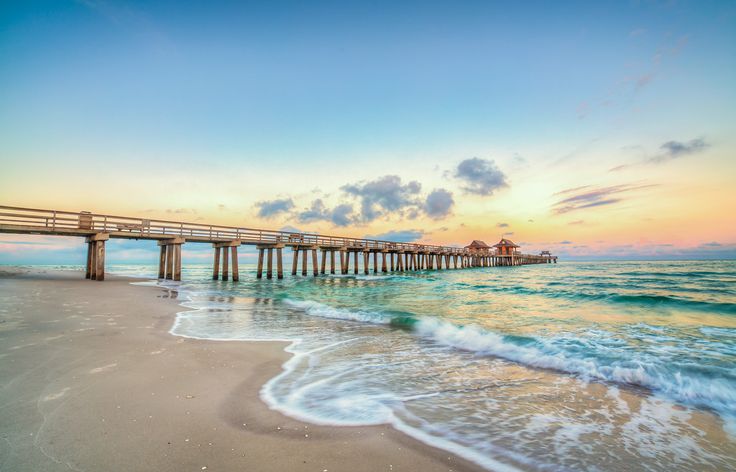 a pier on the beach at sunset with waves coming in