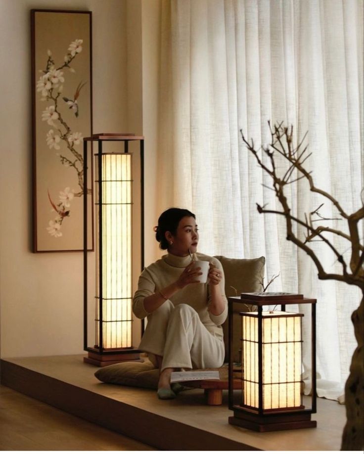 a woman sitting on a couch next to two lamps and a vase with flowers in it