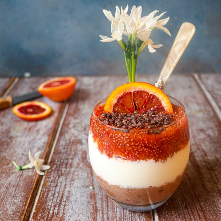 an orange and chocolate dessert with flowers in the center on a wooden table next to sliced blood oranges