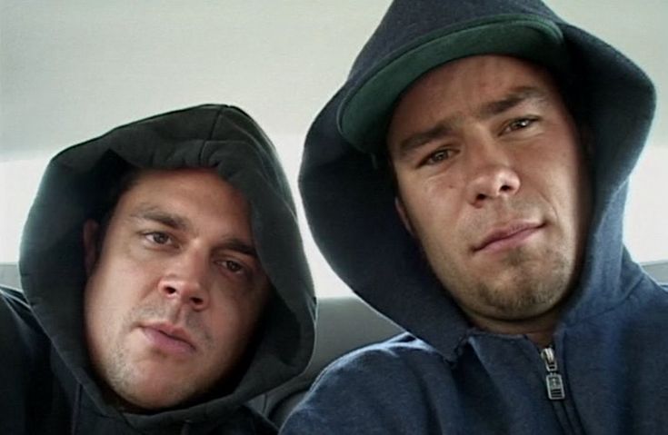 two men sitting next to each other in the back seat of a car wearing hoodies