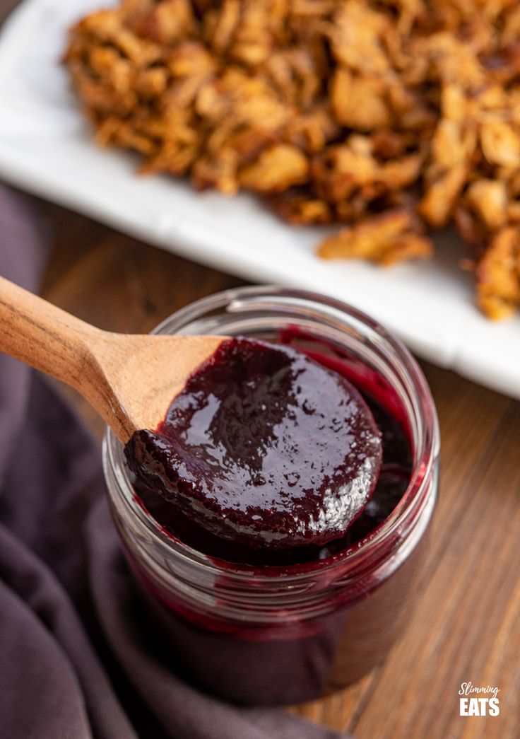 a wooden spoon with jam in it next to some food on a plate and napkin