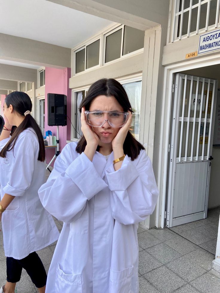 two women in white lab coats are walking down the street with their hands on their faces