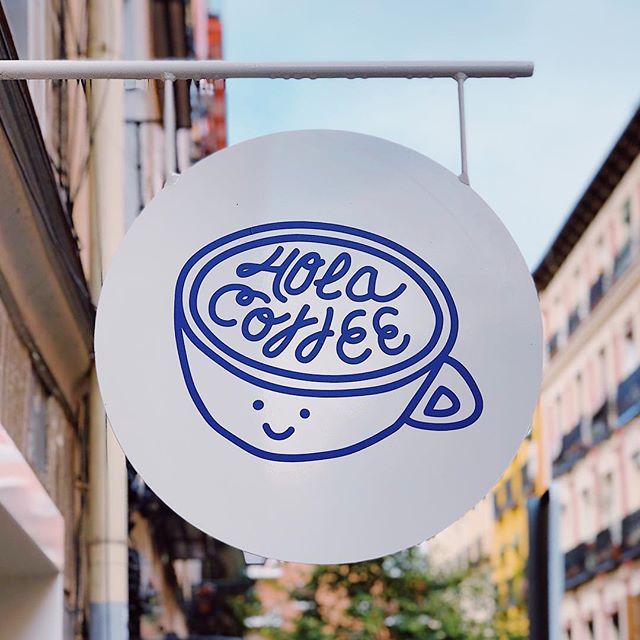 a white sign hanging from the side of a building with blue writing on it that says coffee