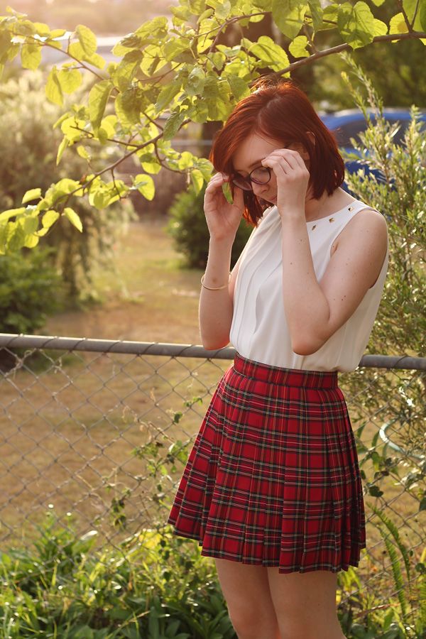 a woman in a plaid skirt talking on her cell phone while standing next to a fence