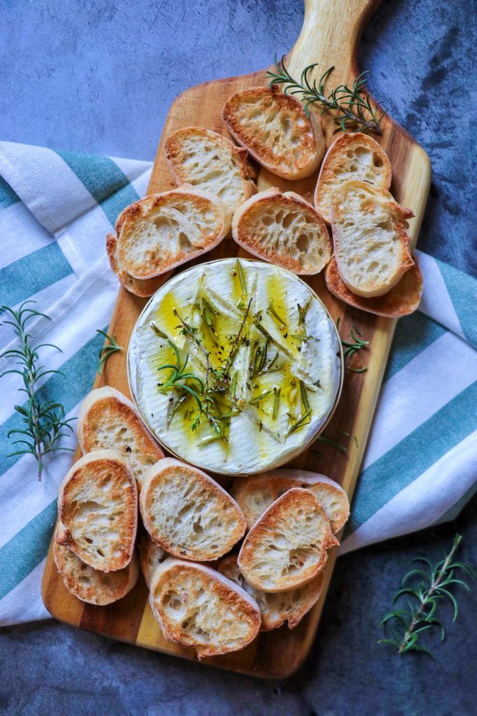 an assortment of breads on a cutting board with cheese and herbs in the middle