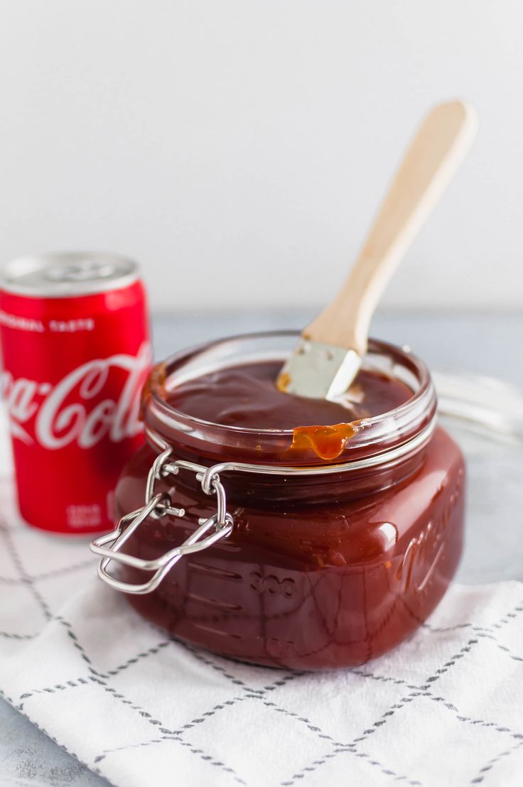 a glass jar filled with chocolate spread next to a can of coca - cola and a wooden spoon