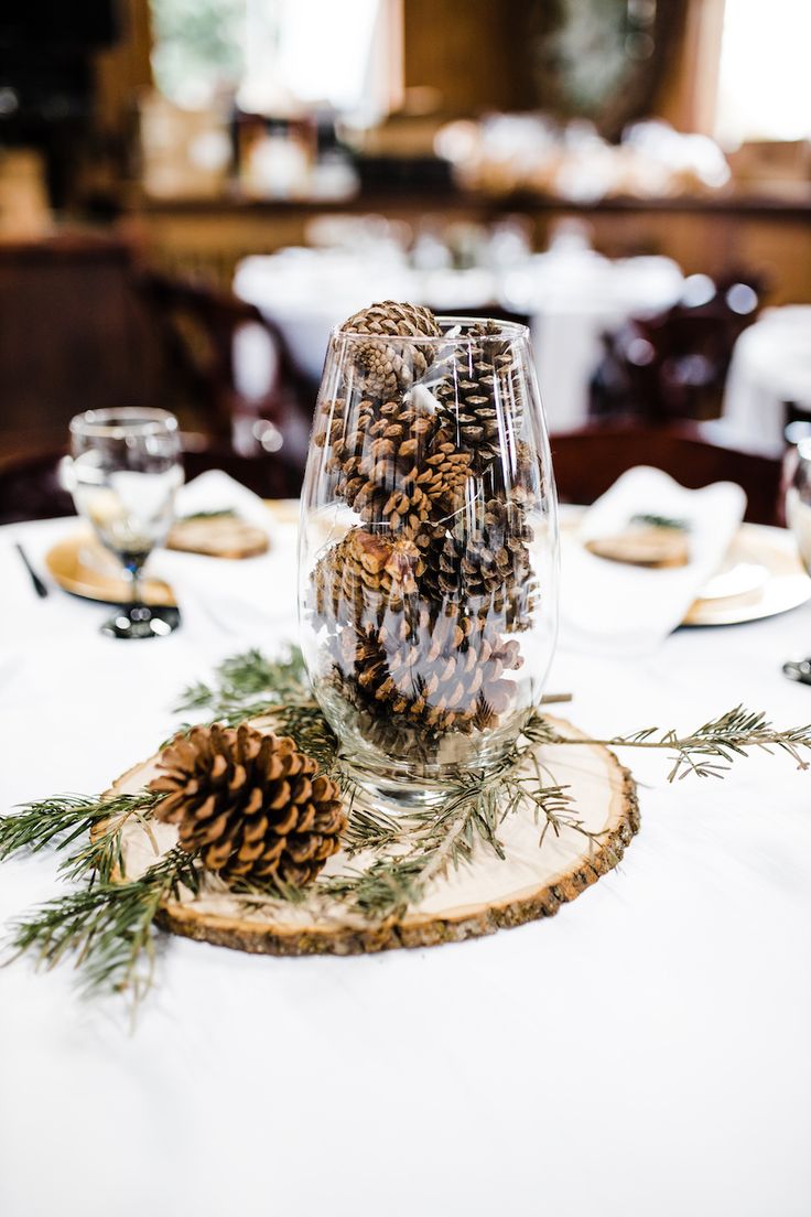 Fairy lights were mixed in with the pinecones to be turned on at night. Wedding Pinecones Centerpieces, November Wedding Reception Decor, Center Piece For Winter Wedding, Winter Wedding Rustic Decor, Winter Wedding Olive Green, Rustic Winter Wonderland Party, Wedding Centerpieces With Pinecones, Winter Wedding Pinecones, Winter Wedding Decorations Rustic