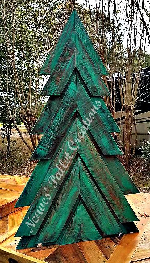 a green wooden christmas tree sitting on top of a wooden pallet in front of some trees