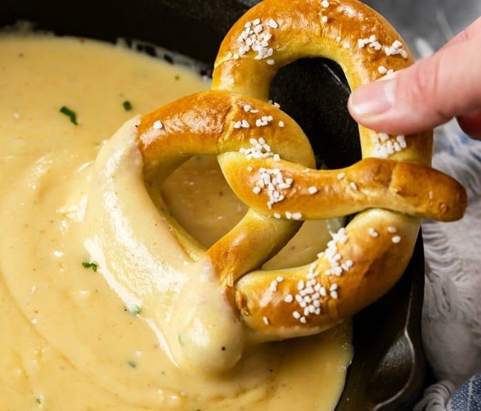 a pretzel being dipped with cheese sauce in a skillet