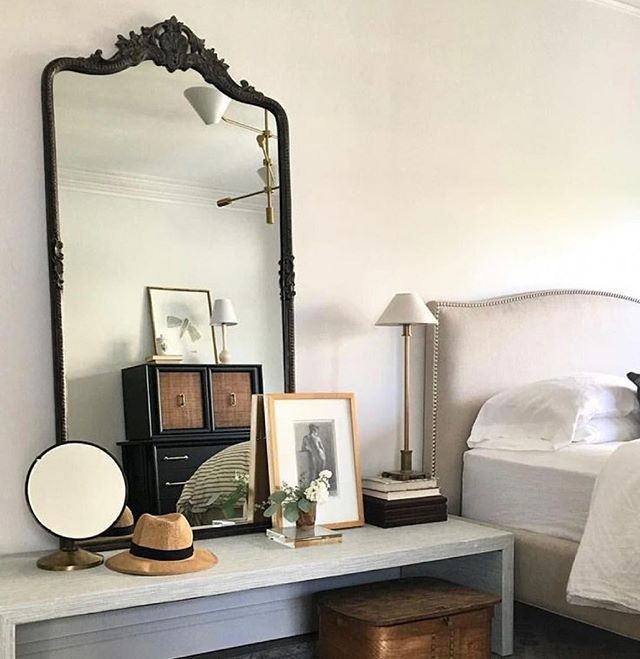 a bedroom with a white bed and a mirror on the wall next to a dresser