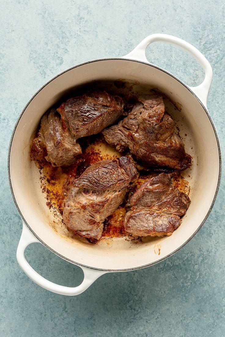 a pot filled with meat sitting on top of a blue counter next to a knife