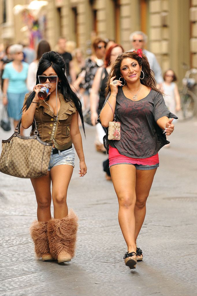 two women walking down the street talking on their cell phones and one is holding a purse