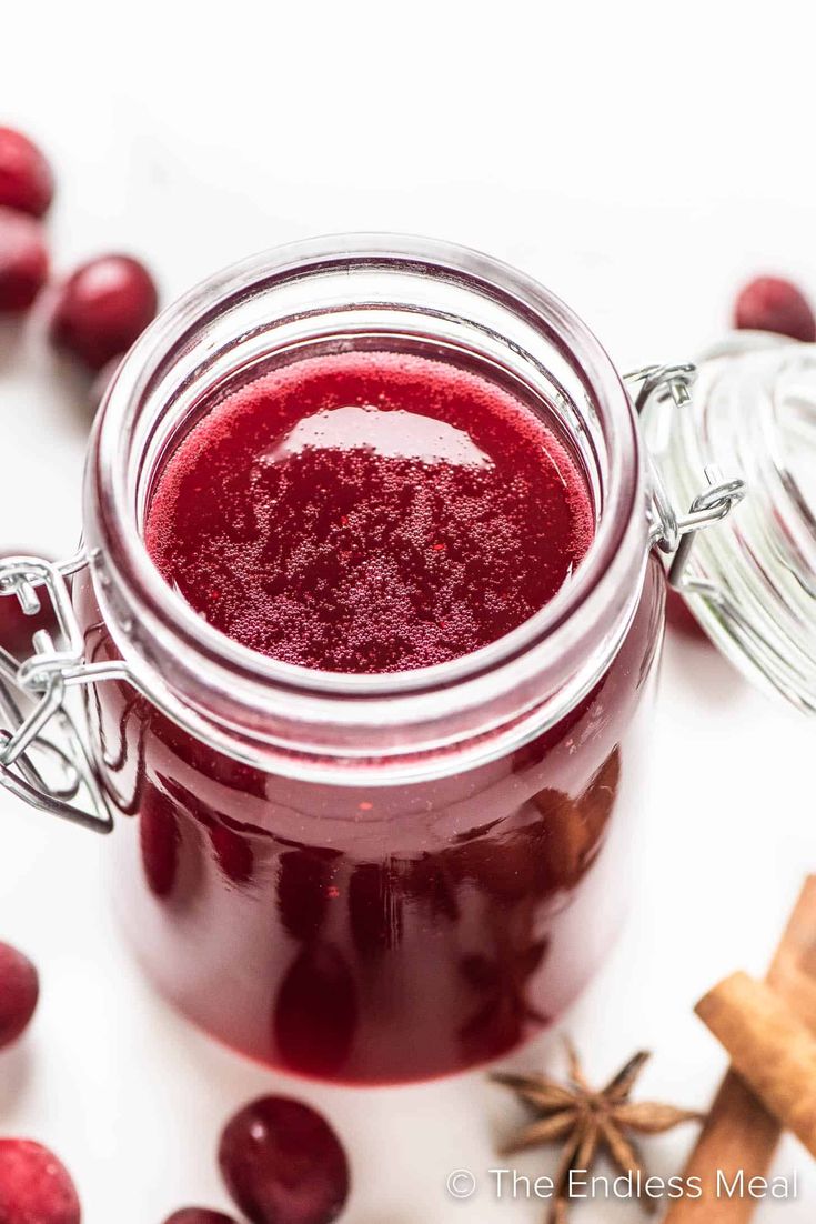 cranberry sauce in a glass jar surrounded by fresh cranberries and cinnamon sticks