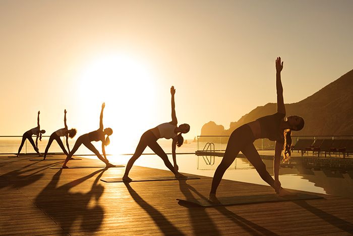 a group of people doing yoga on a dock at sunset with the sun in the background