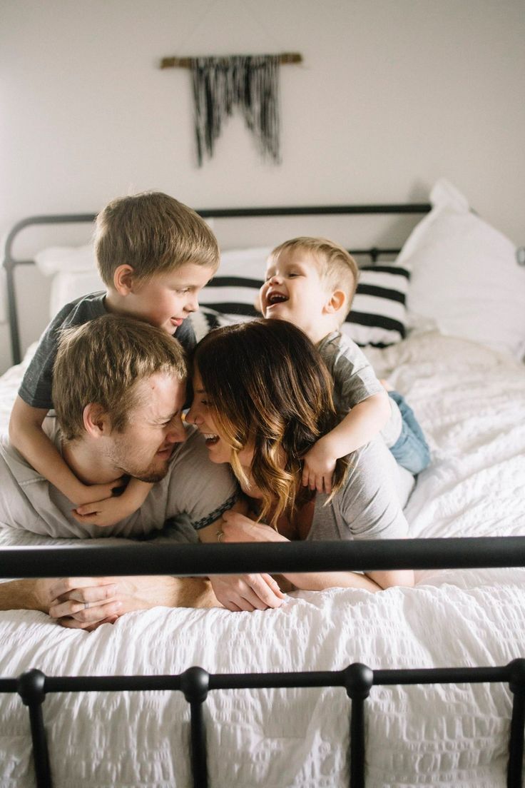 a family is laying in bed together and smiling at each other while the child sits on his mother's shoulders