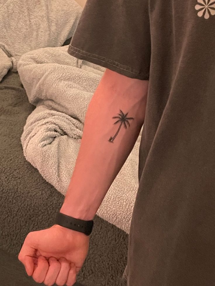 a man with a palm tree tattoo on his arm and wrist is standing in front of a bed