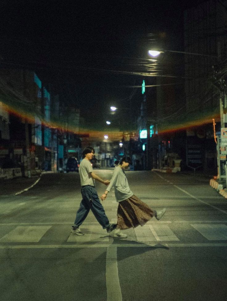 two people crossing the street at night with their hands in each other's pockets