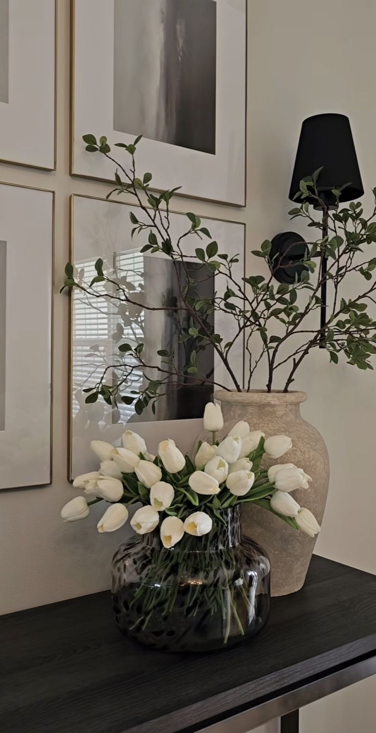 a vase filled with white flowers sitting on top of a table next to framed pictures