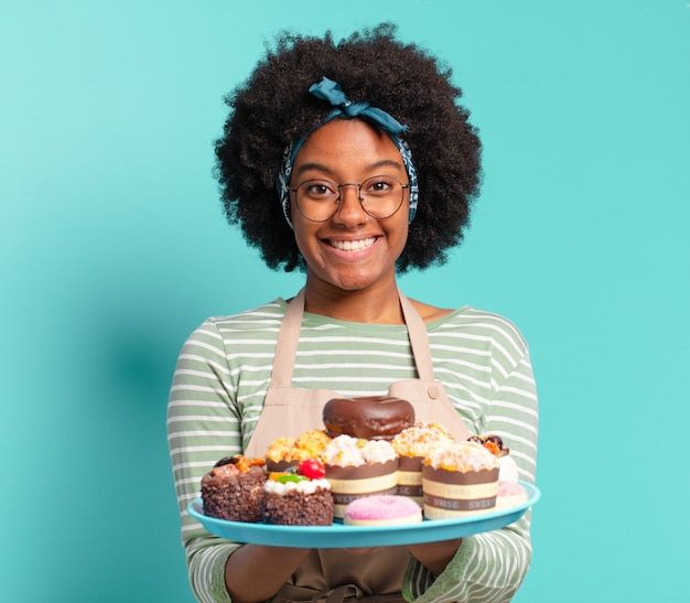 a woman with an apron holding a tray of cupcakes on it's side