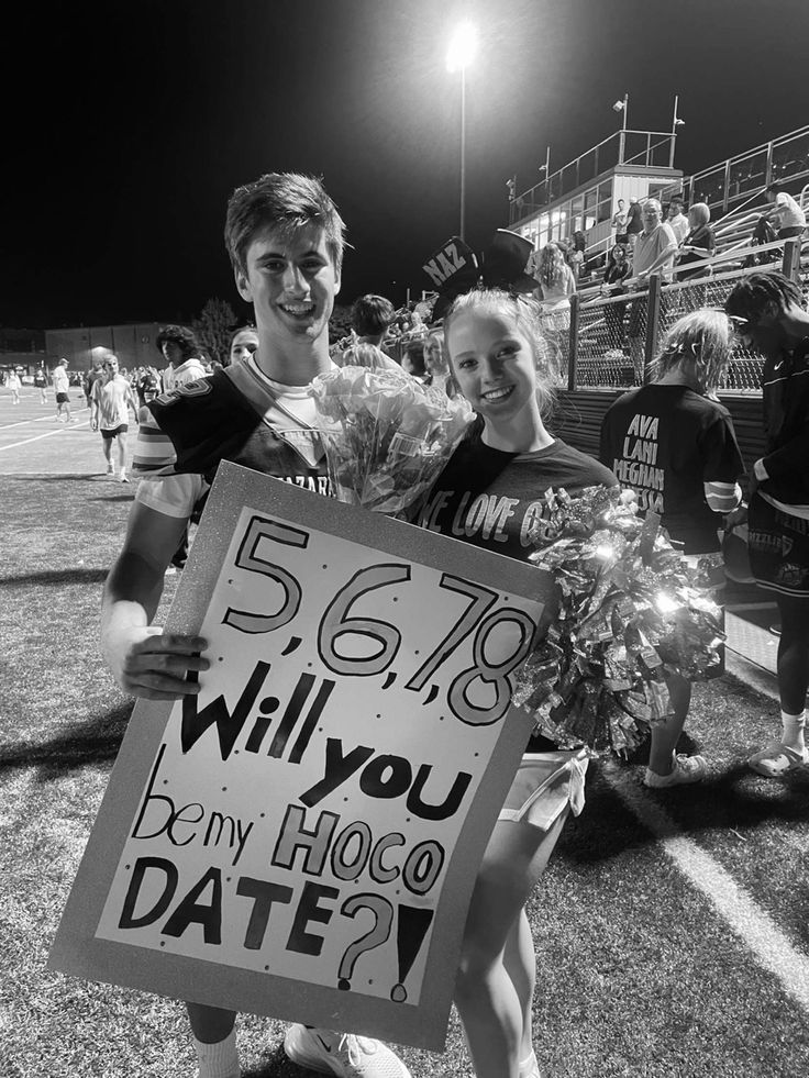 two people holding a sign that says will you be my hogo date?