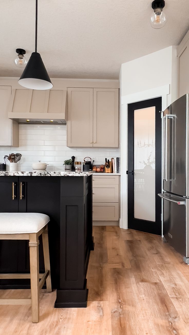 a kitchen with black and white cabinets, wood flooring and an island in the middle