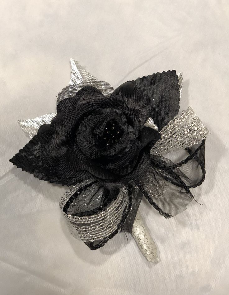 a black flower with silver sequins on it sitting on a white cloth surface