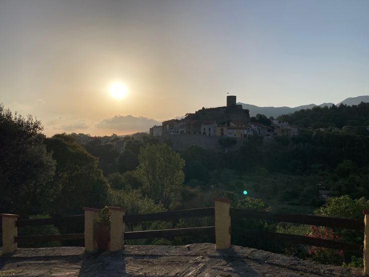 the sun is setting over some hills and houses in the distance with trees on either side