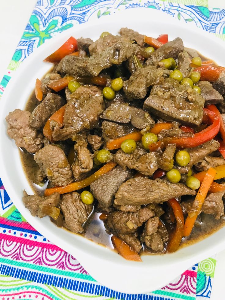 a white bowl filled with meat and vegetables on top of a table cloth next to a fork