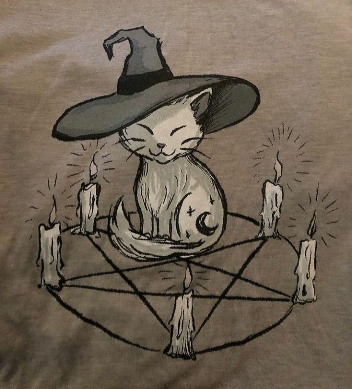 a cat wearing a witches hat sitting on top of a pen and surrounded by candles