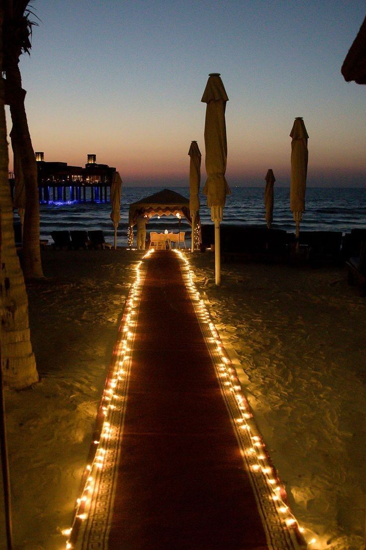 a lighted walkway leading to the beach at night with umbrellas and lights on it