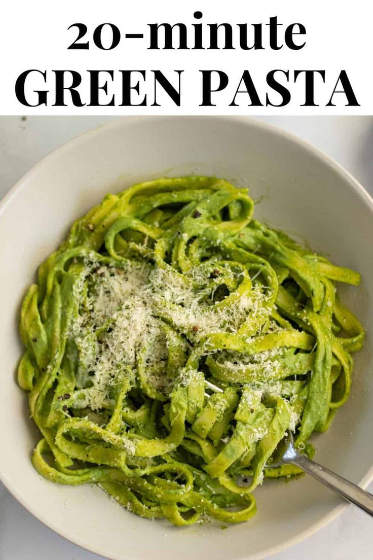 a white bowl filled with green pasta covered in pesto sauce and topped with parmesan cheese