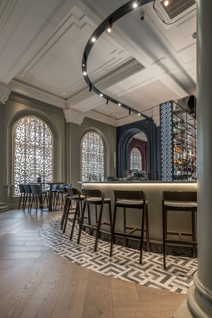 an empty bar with several stools in front of the bar and two large windows