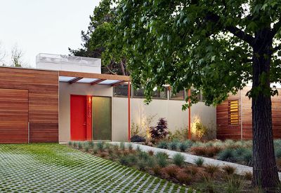 a modern house with an orange door in the middle of a grassy area next to a tree