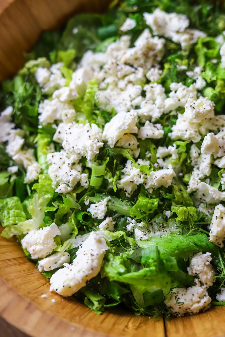 a wooden bowl filled with lettuce and feta cheese on top of it