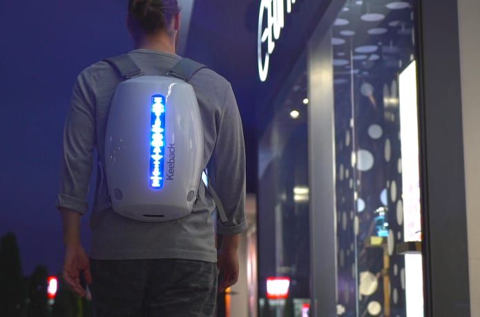 a man is walking down the street with a backpack on his back and an electronic device in front of him