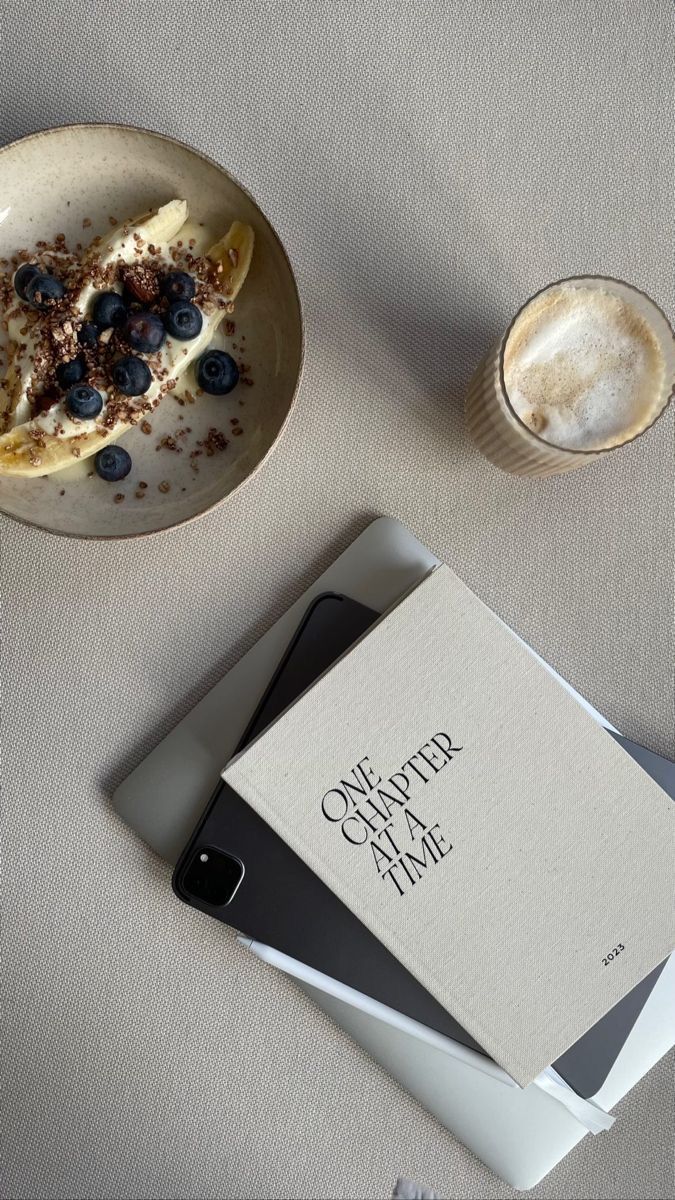 a table topped with a plate of food next to a cup of coffee and an open book