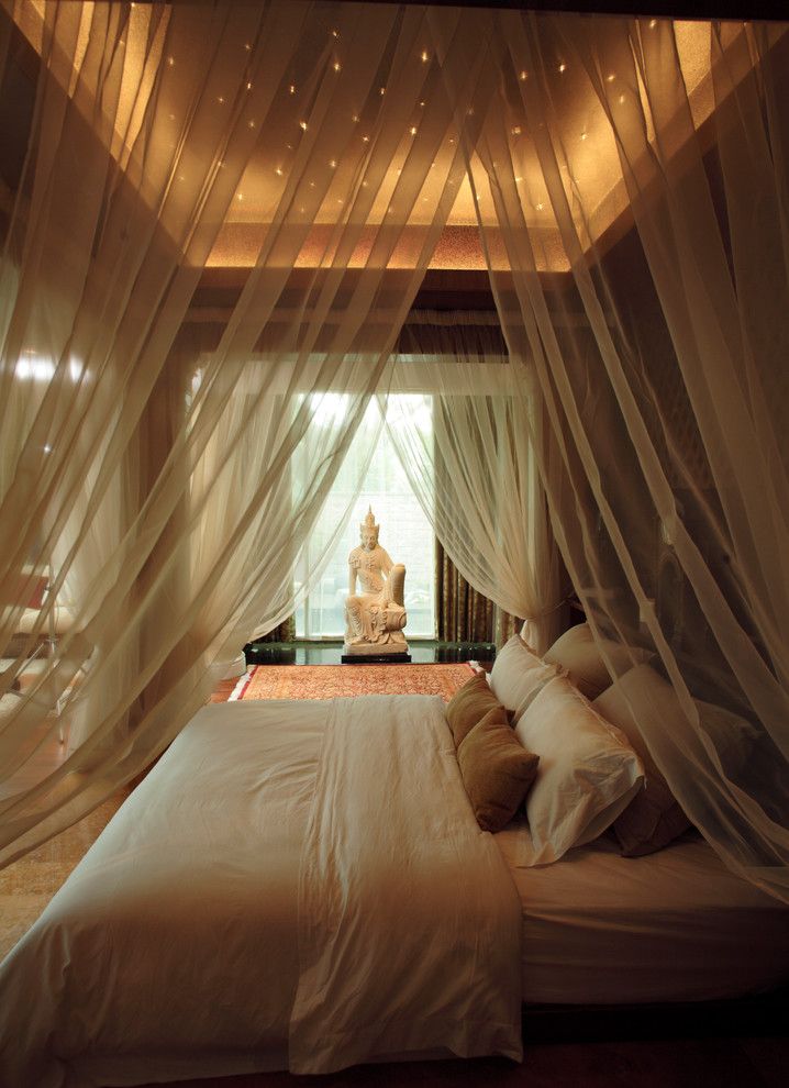 a bed with sheer curtains over it and a buddha statue in the corner on the other side