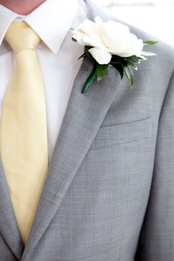 a man in a gray suit with a yellow tie and white flower on his lapel