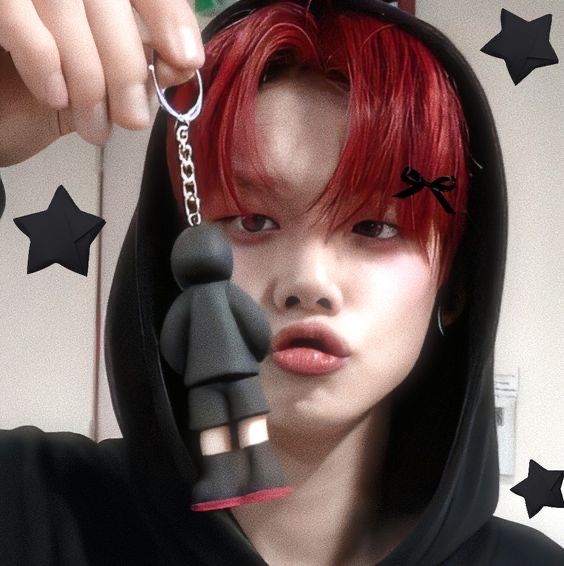 a woman with red hair wearing a black hoodie and holding a pair of scissors in front of her face