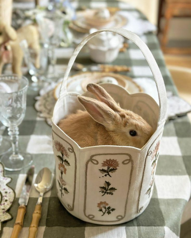 a rabbit sitting in a basket on top of a table next to utensils