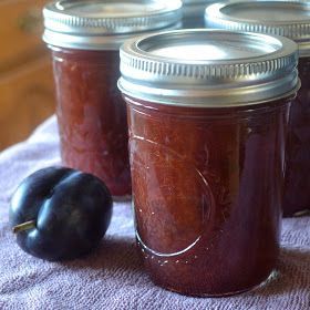 four jars filled with plum jam sitting on top of a purple towel next to an eggplant