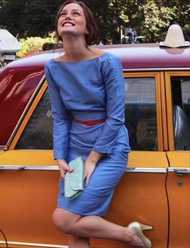 a woman in a blue dress sitting on the hood of a yellow car and smiling