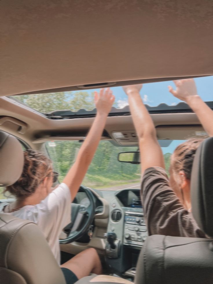 two people sitting in the driver's seat of a car with their hands up