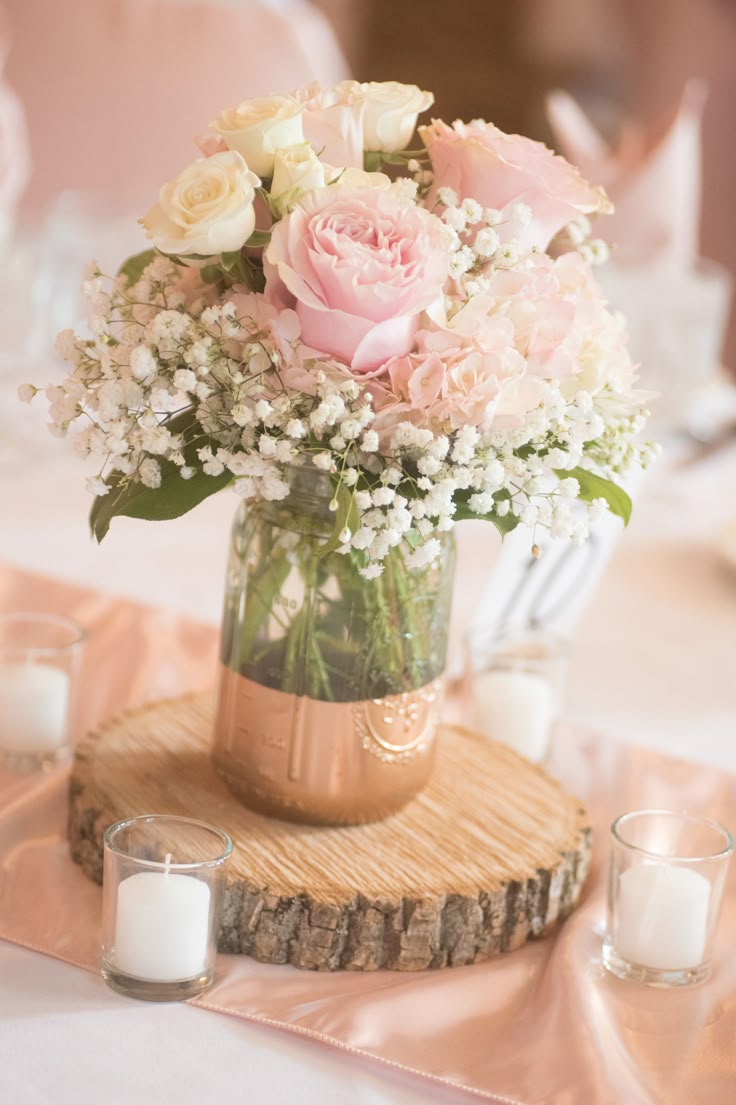 a vase filled with pink and white flowers on top of a wooden table next to candles