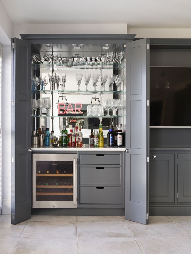 a kitchen with grey cabinets and wine glasses on the glass shelves above the oven door