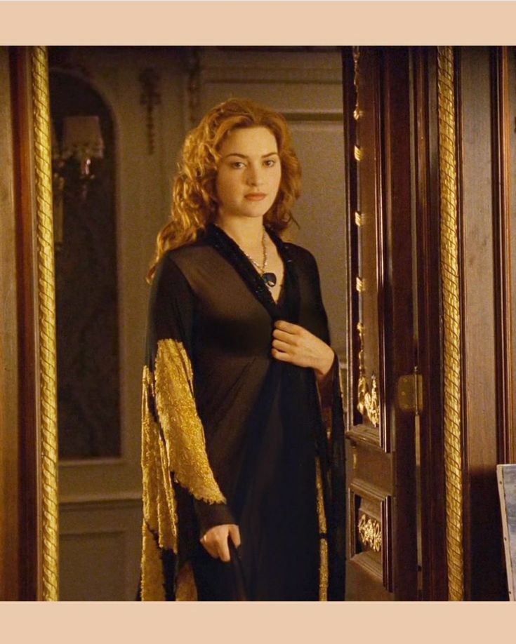 a woman standing in front of a door wearing a black and gold dress with long sleeves