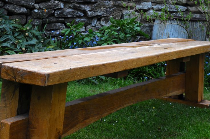 a wooden bench sitting on top of a lush green grass covered park field next to a stone wall