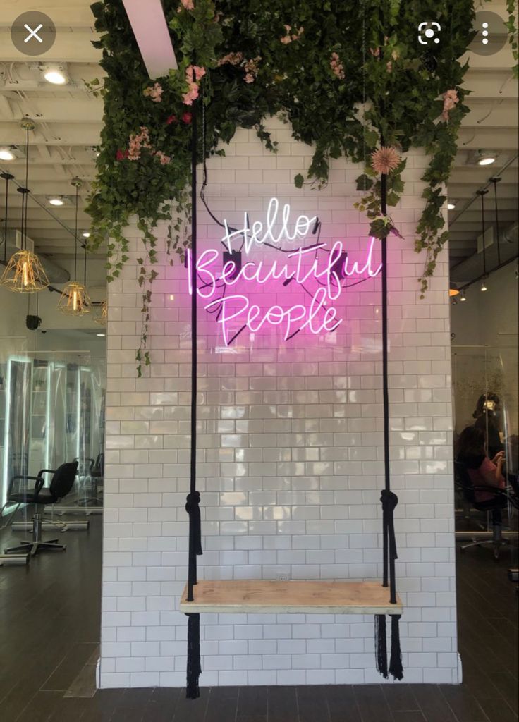 a pink neon sign hanging from the side of a white brick wall next to a wooden bench