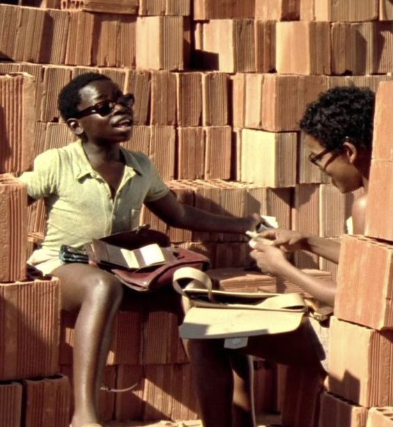 two young men sitting on top of stacks of cardboard boxes and looking at each other